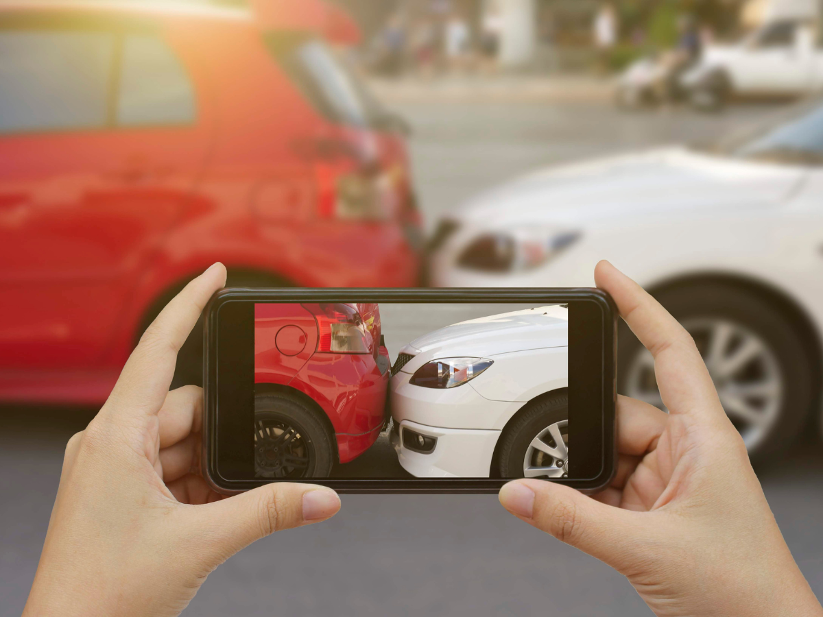 A person taking a photo on their smart phone of a car accident for insurance.