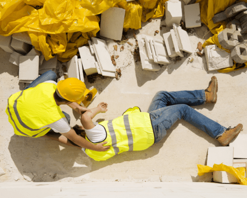 Two construction workers in a construction zone. One is tending to the other who is injured on the ground.