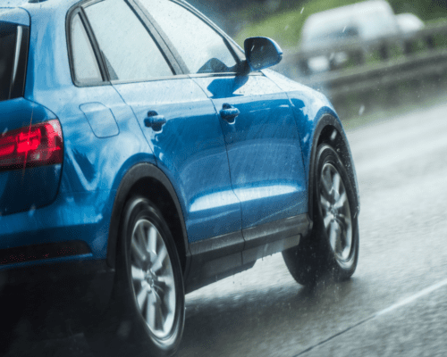 A blue car driving on the freeway in light rain.