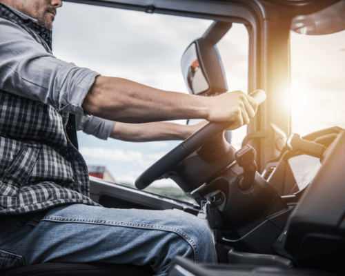 A truck driver from the chin down holding the steering wheel.