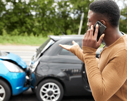 A man on the phone looking at a fender accident behind him.